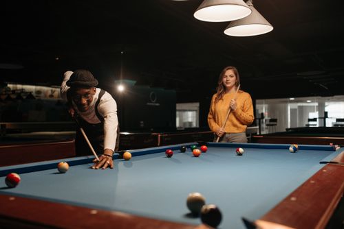 Free A man and woman enjoying a friendly game of billiards in a dimly lit pool hall. Stock Photo
