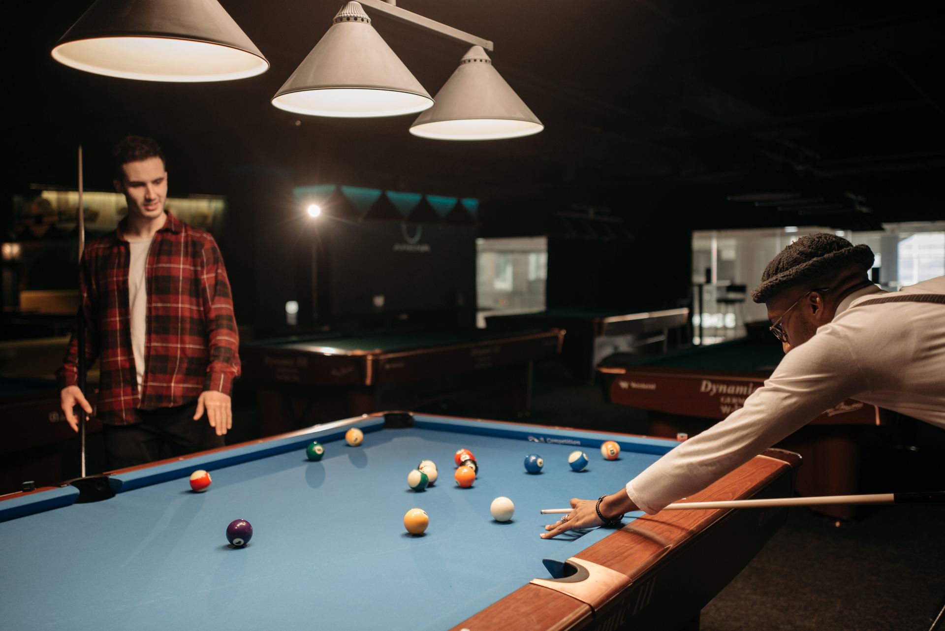 Two men playing pool on a blue table in a dimly lit room, enjoying a leisure activity.