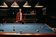 A Man in Checkered Plaid Shirt Holding a Cue Stick