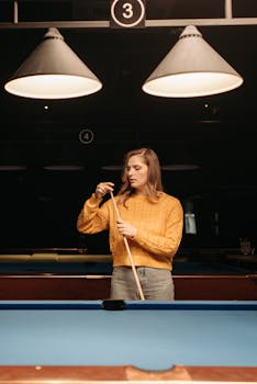 Caucasian woman in a yellow sweater preparing a cue stick at a billiard hall.