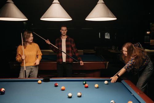 Free Group of friends enjoying a billiards game indoors with cue sticks and balls. Stock Photo
