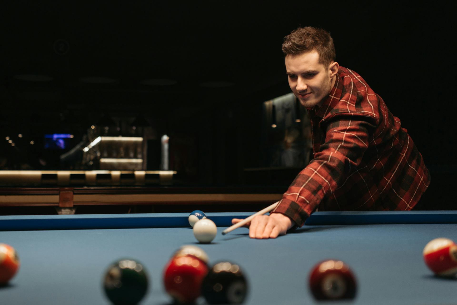 Young man in a plaid shirt playing billiards on a blue pool table indoors.