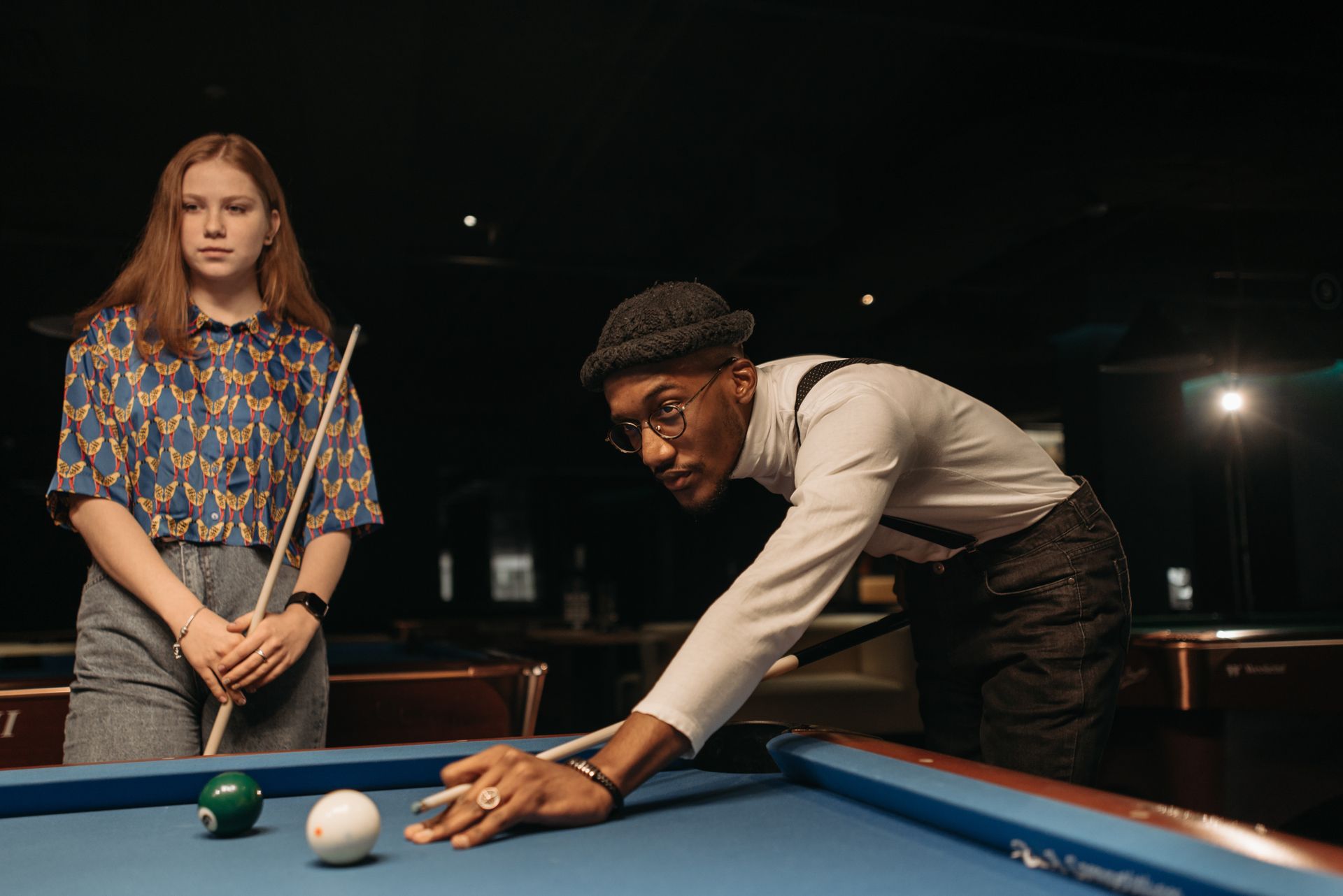 Young adults playing billiards at a pool table indoors, focused and enjoying their game.