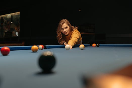 A woman focuses on her shot while playing billiards indoors on a blue pool table.