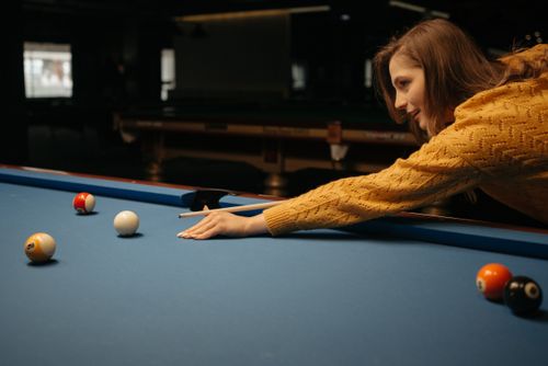 Free A woman in a knitted sweater plays pool on a blue table indoors. Stock Photo