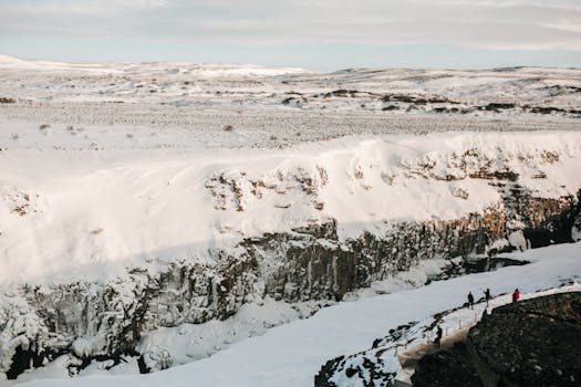 A breathtaking snowy landscape with cliffs and tiny figures walking below in winter.