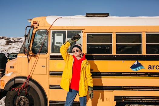 Woman in bright winter clothing posing by a snowy bus in Iceland.