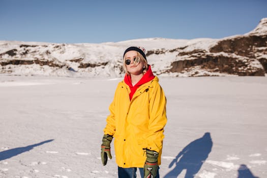 A woman in a yellow jacket and sunglasses stands in a snowy landscape, enjoying the winter sun.