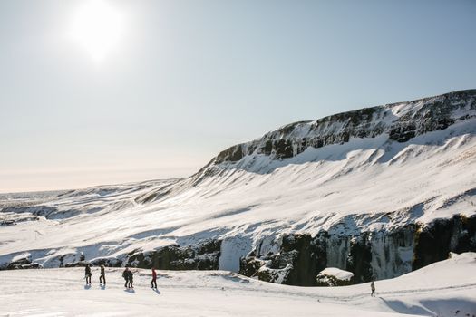 Group of hikers trekking through a snow-covered Icelandic landscape under bright sun.