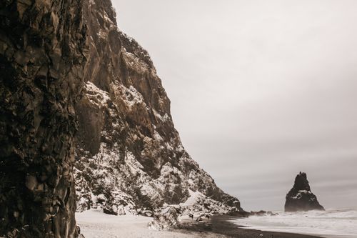 Free A dramatic view of snow-covered cliffs meeting an ocean under a moody sky. Stock Photo