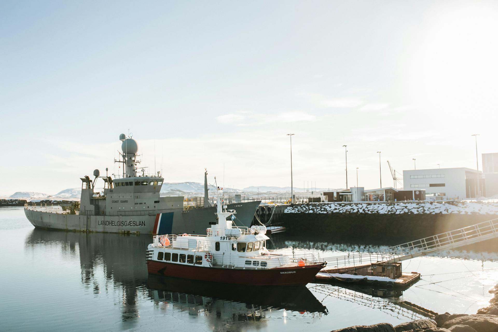 Tranquil harbor scene featuring Icelandic Coast Guard vessel and docked boats under clear skies.