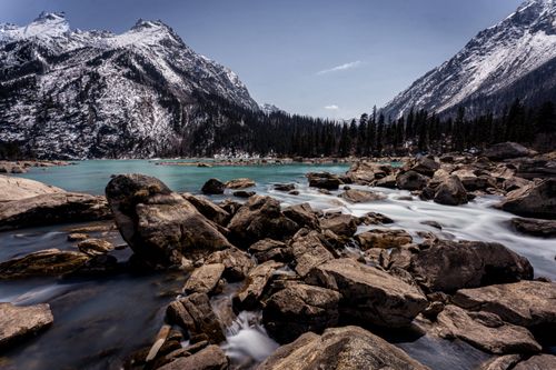 Free Breathtaking view of a turquoise river flowing through a rocky landscape with snow-capped mountains. Stock Photo