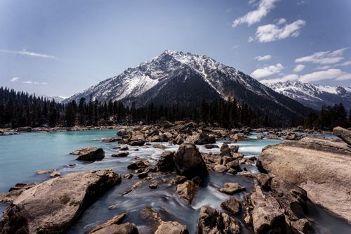 Free Stunning mountain landscape with flowing river and forest backdrop. Stock Photo
