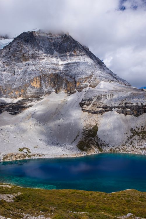 Free Majestic mountain towering over a vibrant blue lake amidst cloudy skies. Stock Photo