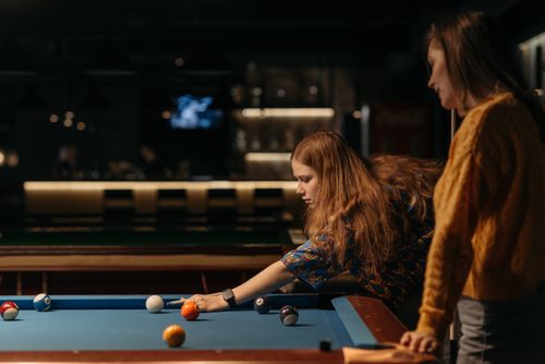 Free Two women playing billiards in a dimly lit room, engaged and focused on the game. Stock Photo