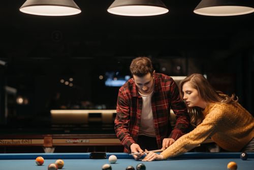 Free A young couple enjoys learning billiards together in a warmly lit room, sharing a recreational moment. Stock Photo