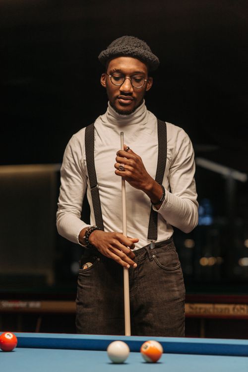 Free Man with eyeglasses and facial hair holding a cue stick at a billiard table indoors. Stock Photo