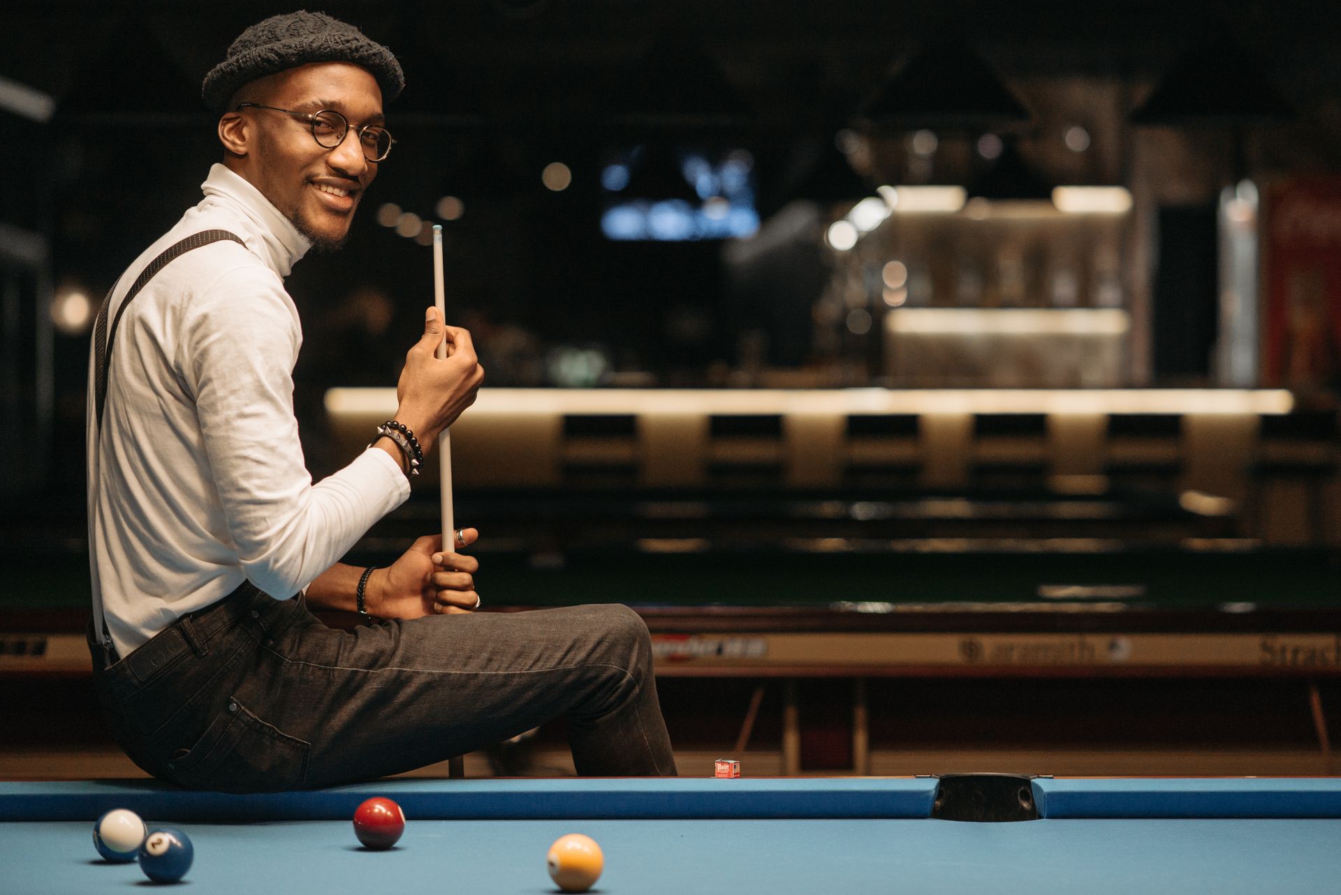 Confident man smiling and holding cue stick on pool table indoors.