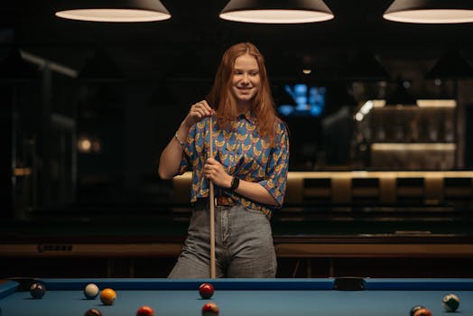 Smiling woman playing billiards indoors, holding cue stick at a pool table.