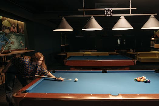Woman enjoying a game of billiards in a dimly lit indoor setting, aiming at the balls.
