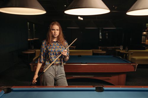 Free Woman with a cue stick standing in a billiard room preparing to play pool indoors. Stock Photo