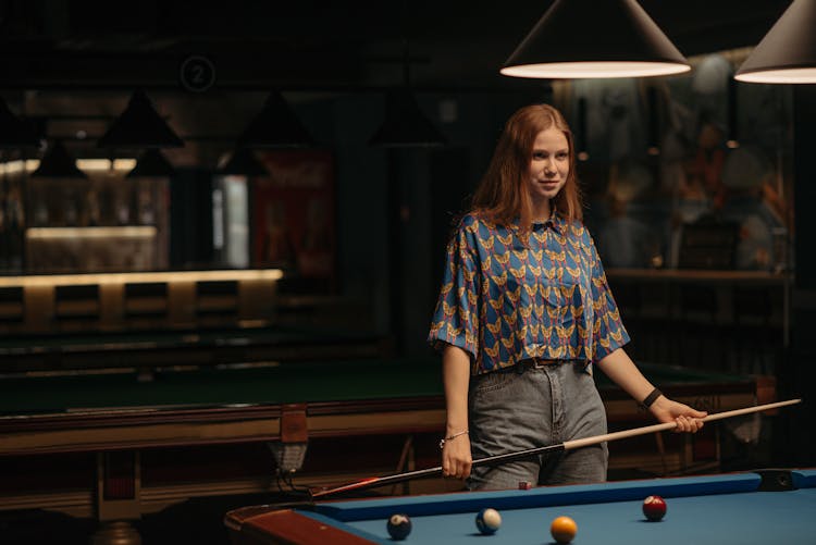 A Young Woman Standing By A Billiard Table Holding A Cue 