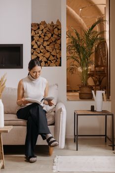 Woman sitting on sofa reading in a stylish living room with firewood and plants.
