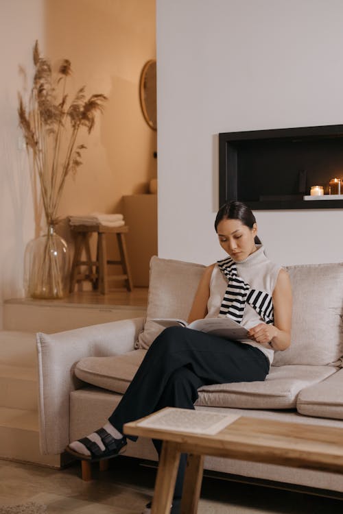 Free A Woman Reading a Magazine while Sitting on the Sofa Stock Photo