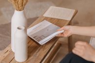 A person reads a magazine on a wooden bench beside ceramic vases, showcasing minimalist decor.
