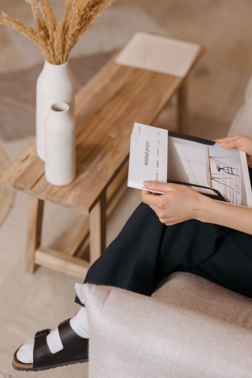 Free A person holding a magazine in a cozy Scandinavian-style living room with vases and wooden furniture. Stock Photo