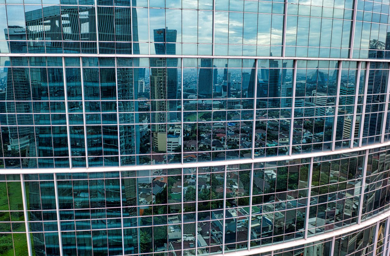 Glass facade of a skyscraper reflecting the cityscape of Jakarta, Indonesia on a clear day.