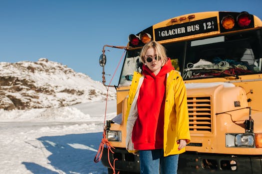 A trendy woman poses in winter attire next to the Glacier Bus on a snowy day.