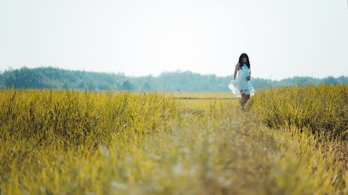 Depth of Field Photography of Woman Wearing White Sleeveless Dress Standing on Green Grass Field