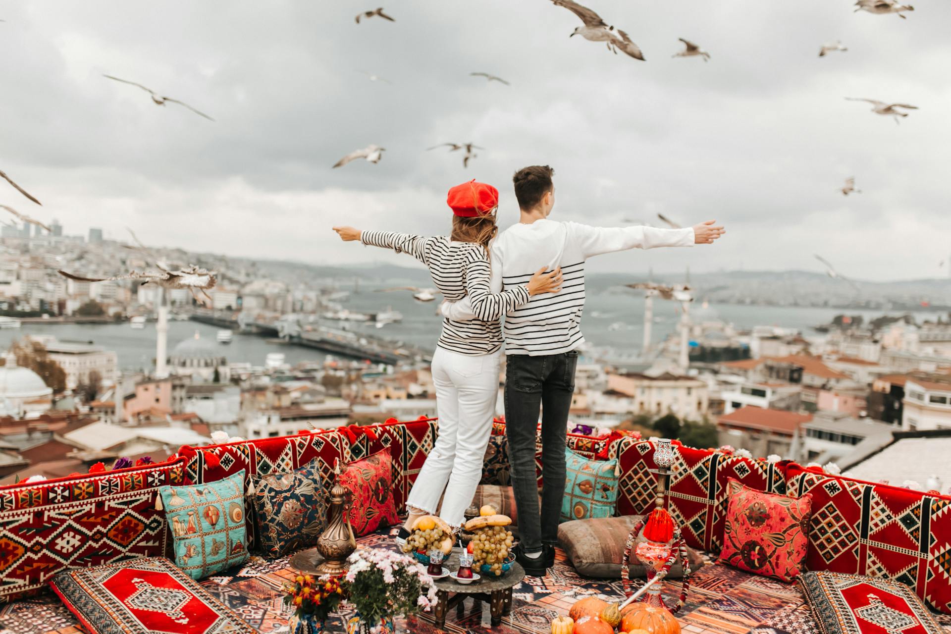 Couple embracing on a colorful Istanbul rooftop with seagulls and cityscape in the background.