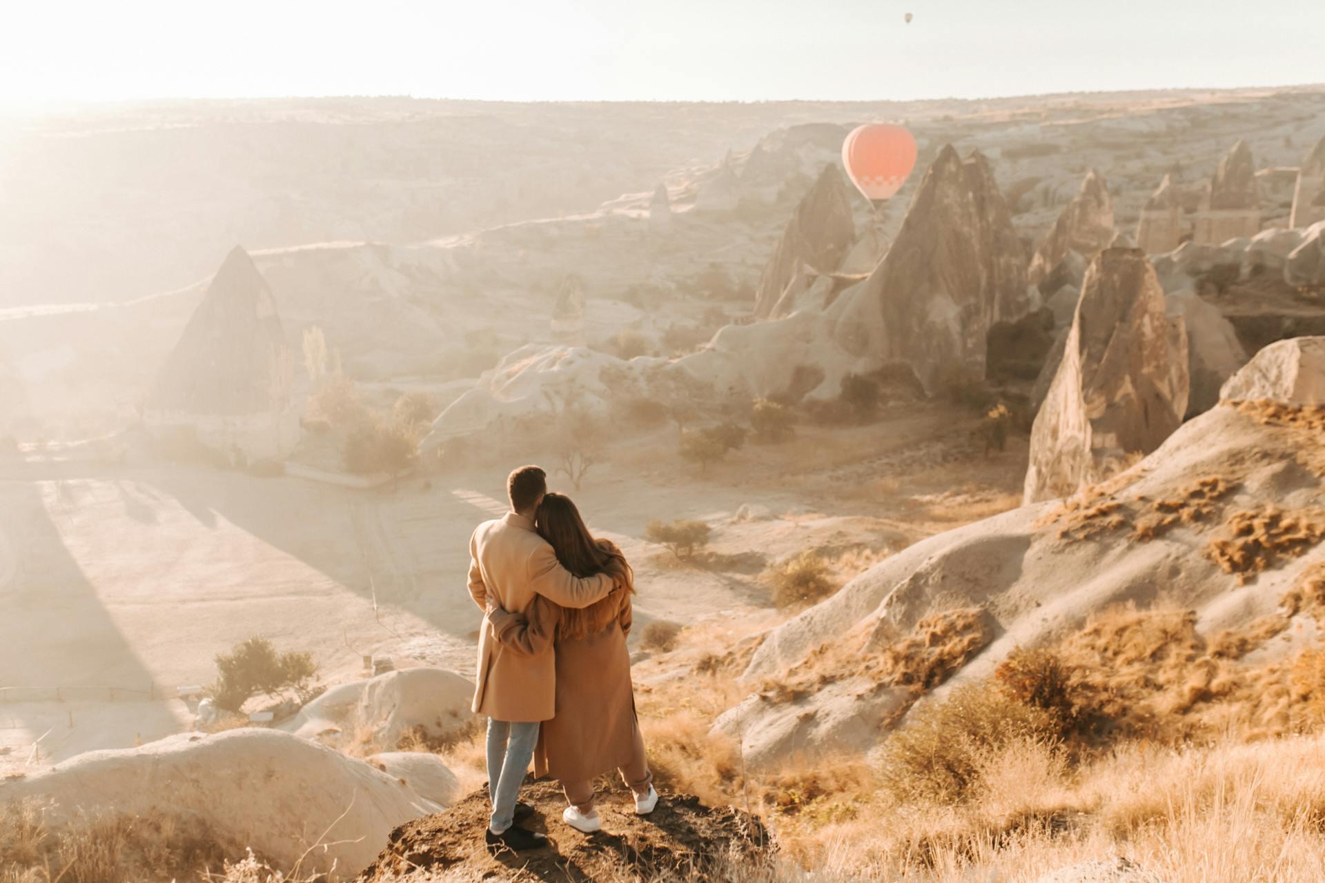 A couple embraces, admiring hot air balloons over Cappadocia's rock formations at sunset.