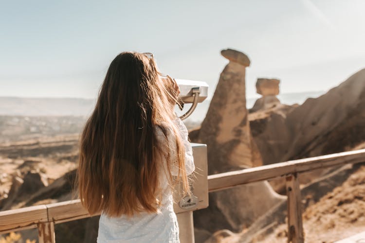 Back View Of A Woman Using A Stationary Telescope At A Viewpoint 