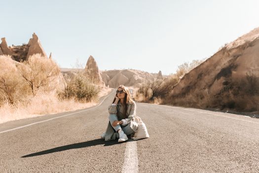 A woman sitting on an empty road in Cappadocia, Turkey with mountainous backdrop.