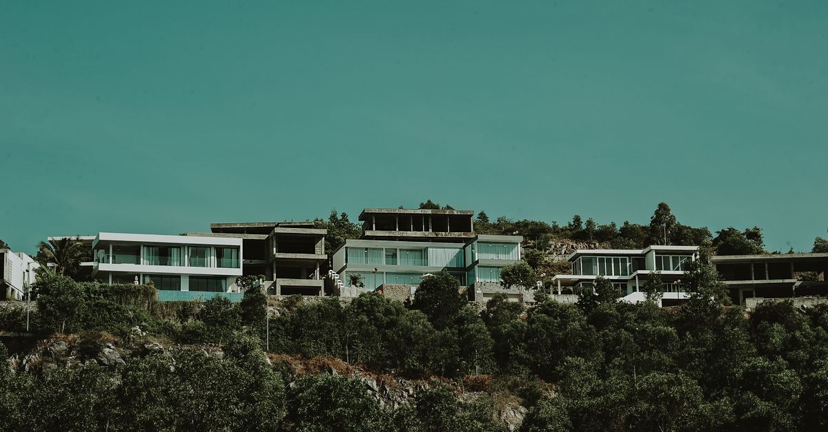 Contemporary hillside villas surrounded by lush greenery under an expansive sky.