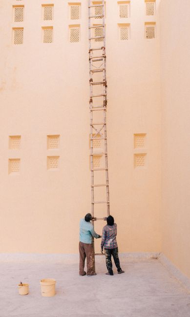 Two men adjust a bamboo ladder against a high wall, showcasing teamwork and effort.