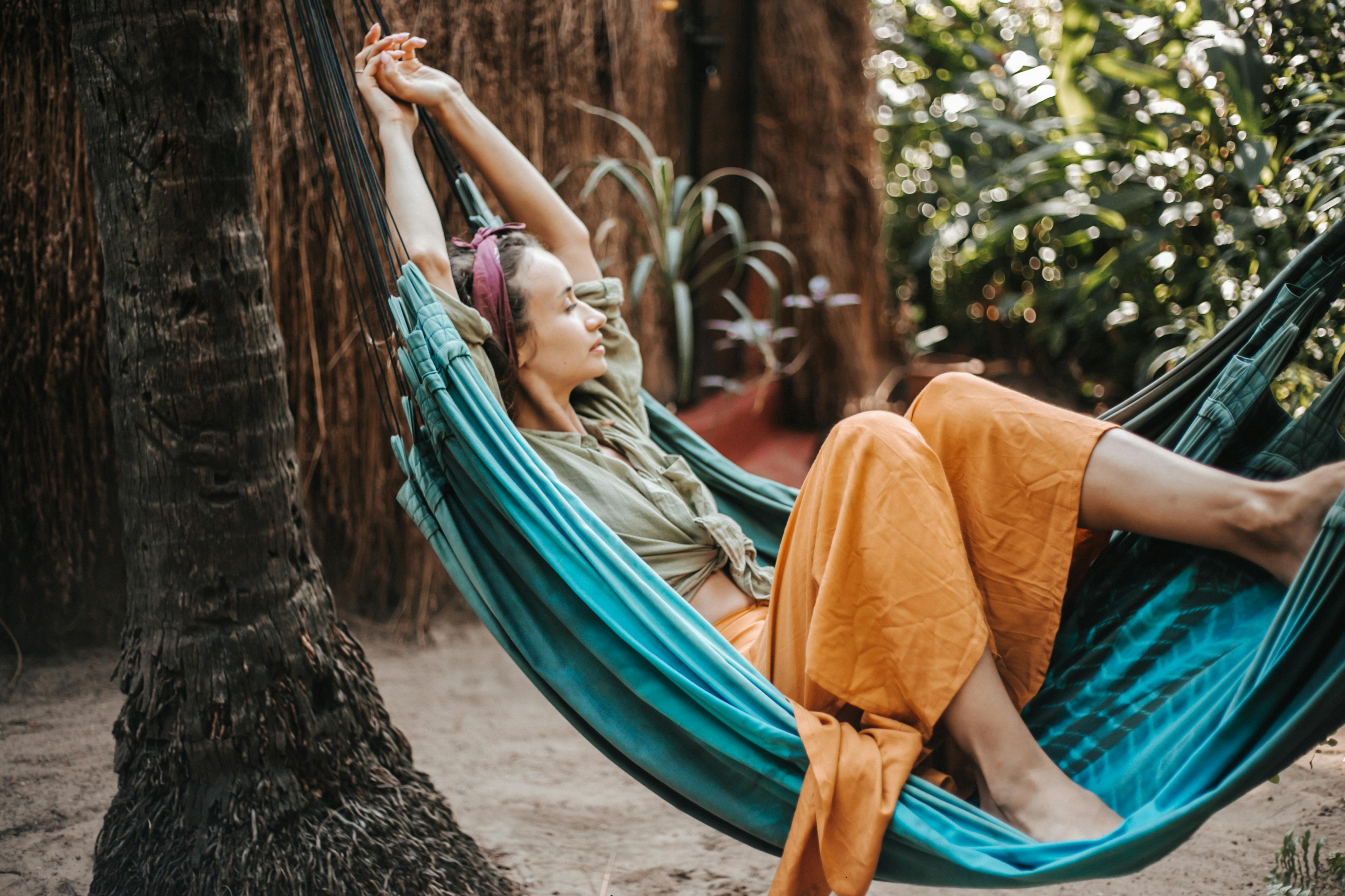 A woman peacefully resting in a hammock surrounded by lush greenery and palm trees.