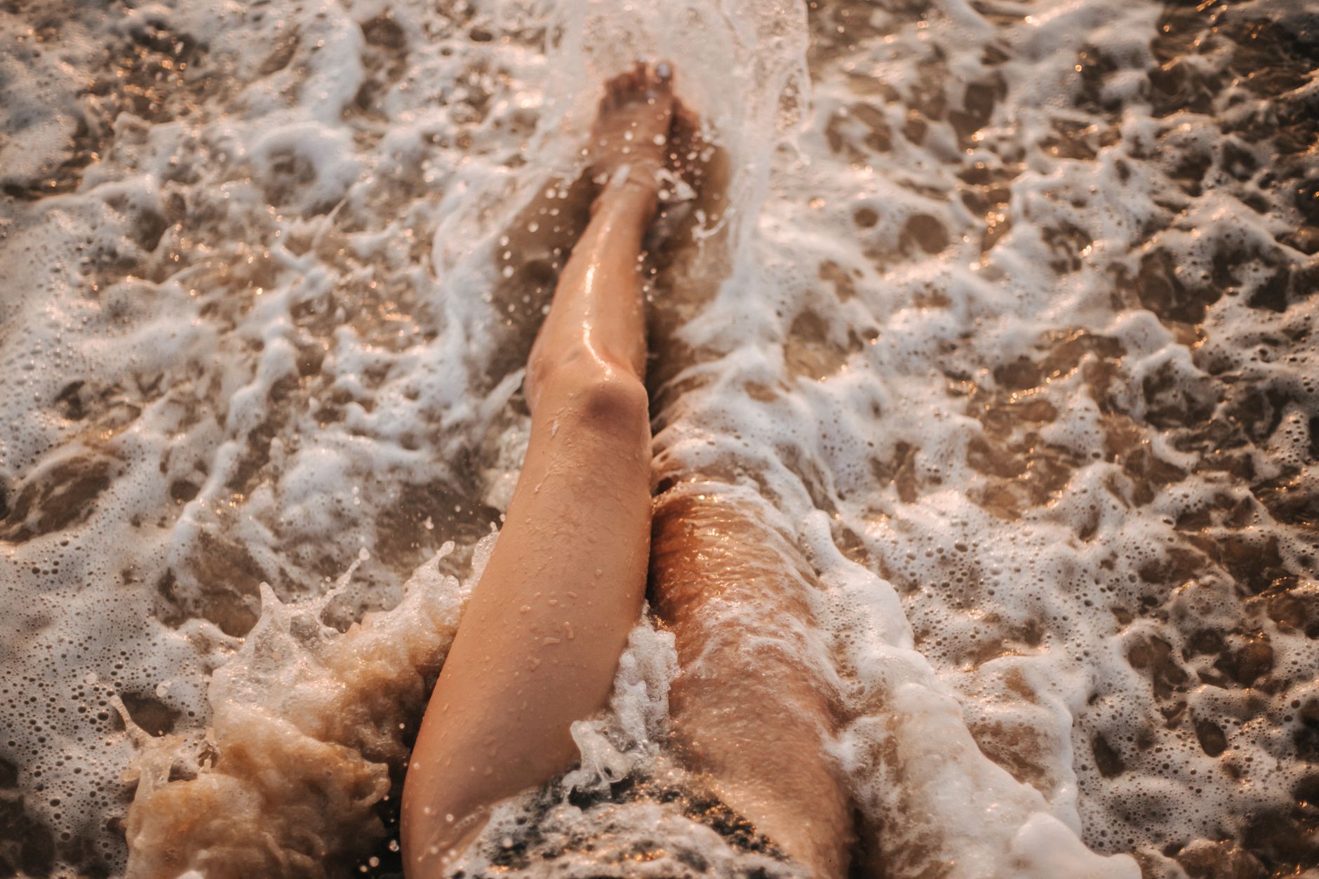 Close-up of legs in foamy ocean waves on a summer beach vacation.