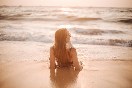 Woman in swimwear relaxing on a sandy beach at sunset, enjoying the serene ocean waves.