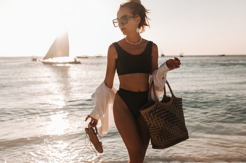 Free Young woman in swimwear with a bag strolling on a beach at sunset. Stock Photo