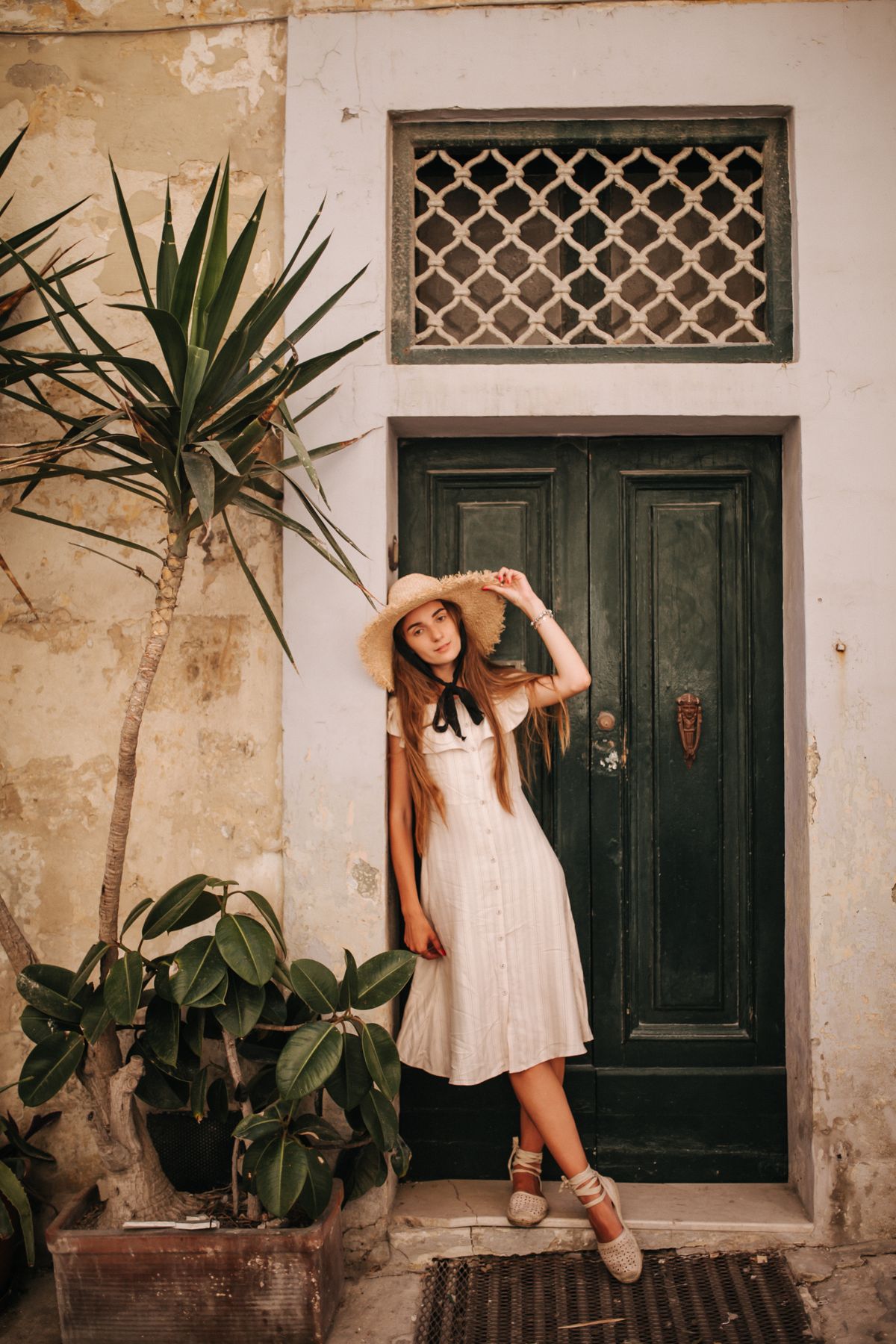 A woman in white leaning on a wall by a door — the editorial chic of a summer afternoon