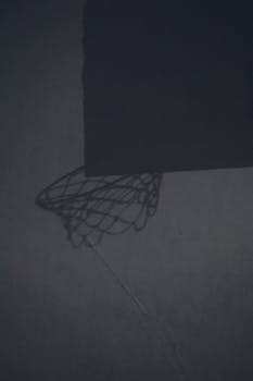 Black and white shadow of basketball hoop with net on concrete wall on public sports ground with sunlight on street