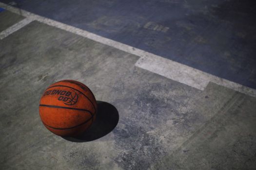 From above of basketball ball with inscription placed on sports ground with marking line on sunny summer day on street