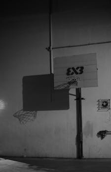 Black and white image of an urban basketball hoop casting shadows on a concrete wall.