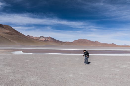 A solitary man explores the vast, dry landscape of Salar de Uyuni under a clear blue sky.
