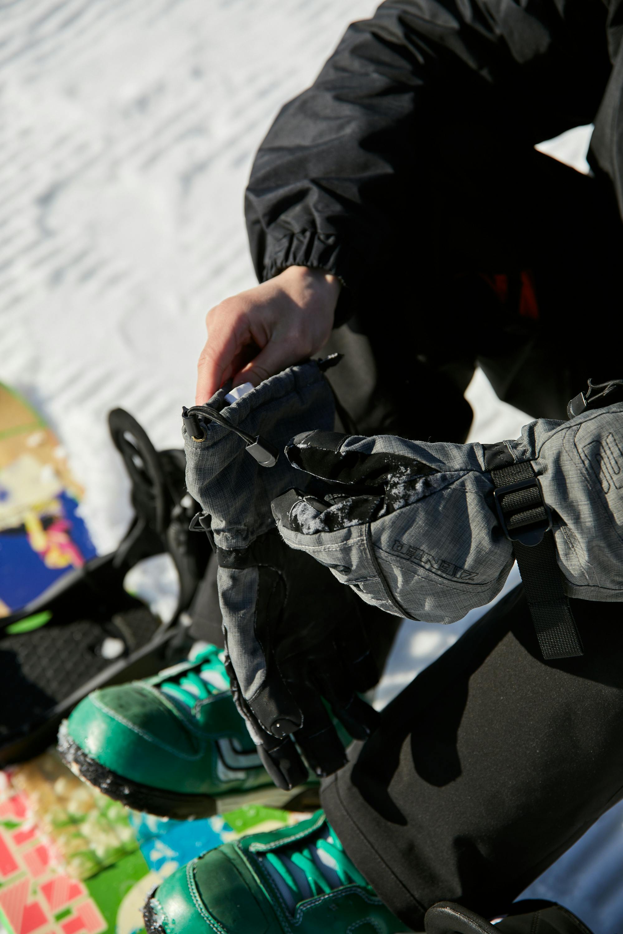 Prescription Goggle Inserts - Person sitting on snow with snowboard, adjusting gloves in bright winter daylight.