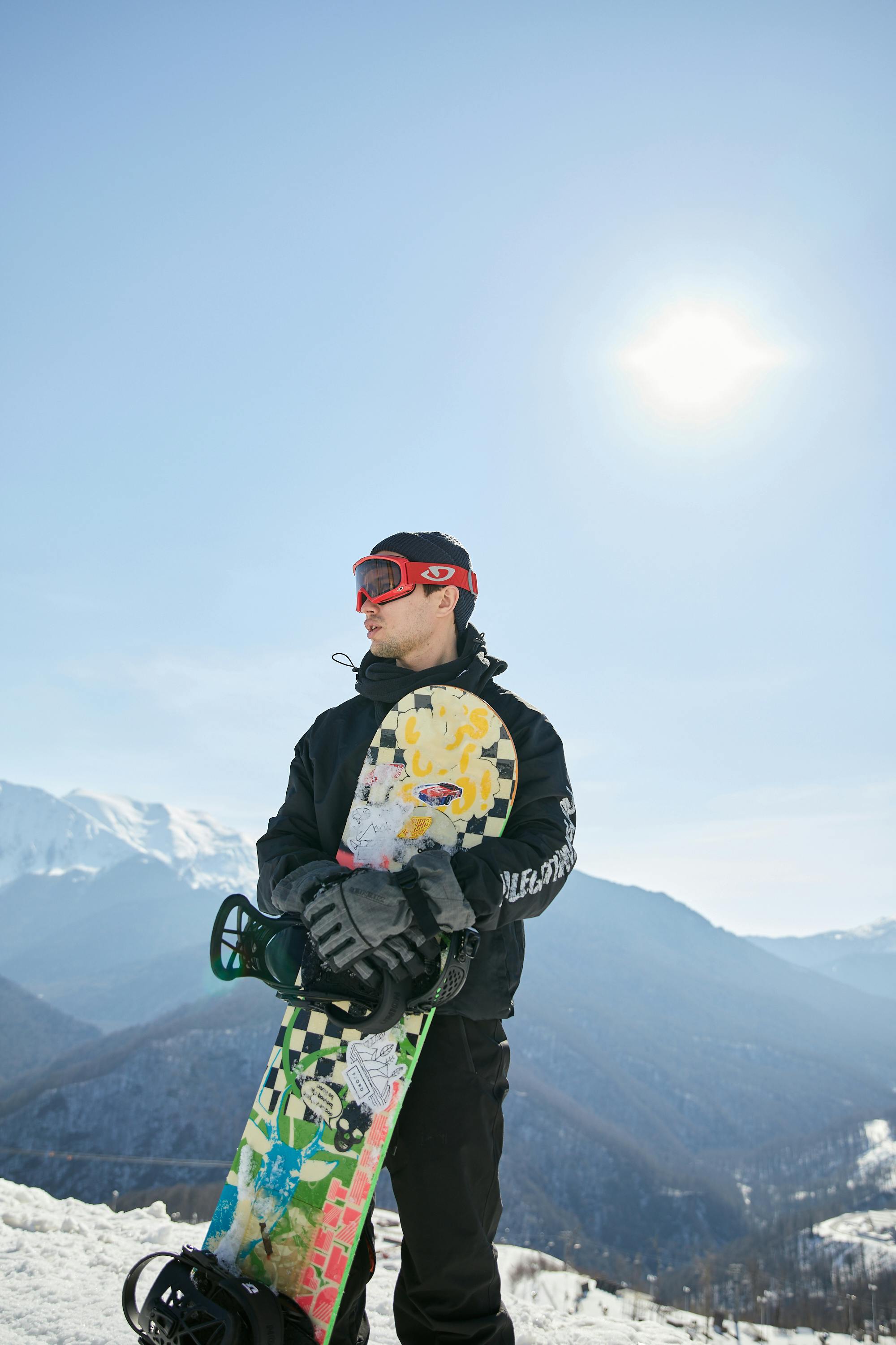 Prescription Goggle Inserts - Adult snowboarder in winter gear with colorful snowboard at snowy mountain resort under bright sun.